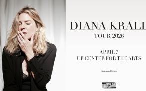 diana krall with hand over mouth in front of a blank curtain.