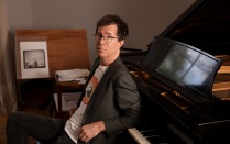 ben folds leaning back on a piano with elbows on the keys. 