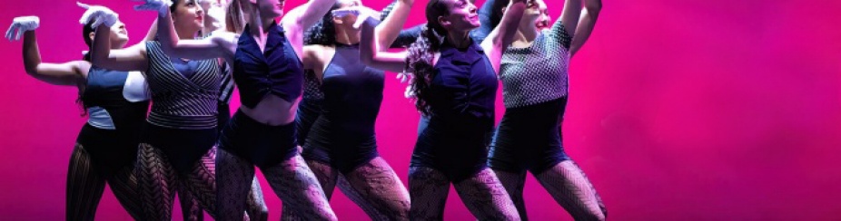 A group of dancers together in front of a hot pink background. 