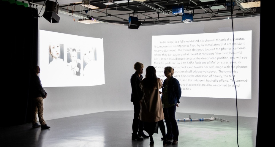 Three people in a dark screening room with projections on two walls.
