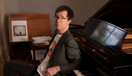 ben folds sitting on piano bench leaning back on grand piano. 