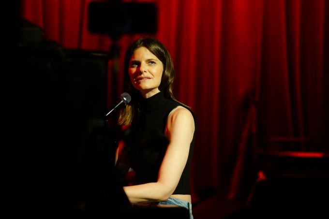 lindsey kraft sitting at a piano in front of a velvet curtain. 