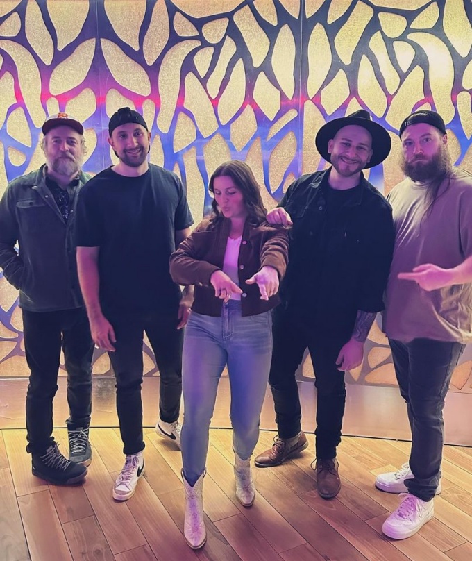 members of voyagr standing on a hard wood floor in front of painted art wall. 